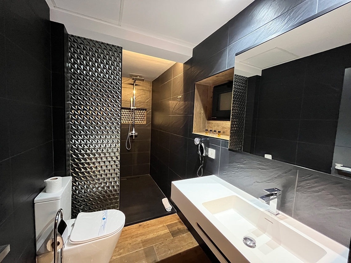 Modern bathroom at Hotel Villa Albero: shower, sink, and toilet with black tiles and wood.