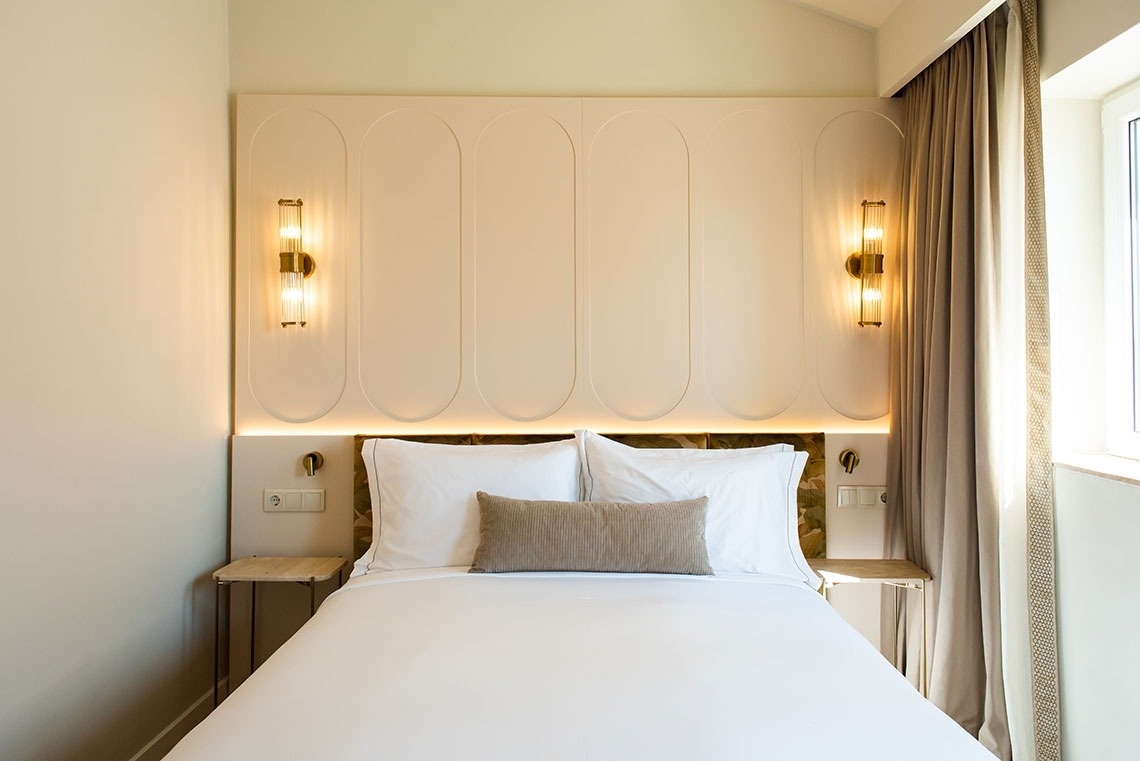 Quarto de hotel contemporâneo com cama confortável, cabeceira elegante e iluminação acolhedora.