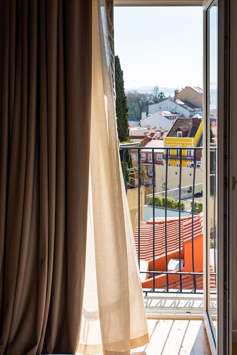 Quarto de hotel com varanda, vista panorâmica da cidade, telhados coloridos e rio.