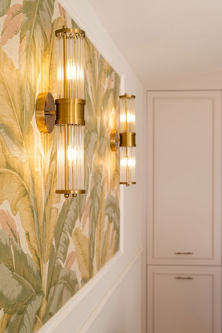Arandelas douradas e papel de parede botânico em hall de hotel elegante.