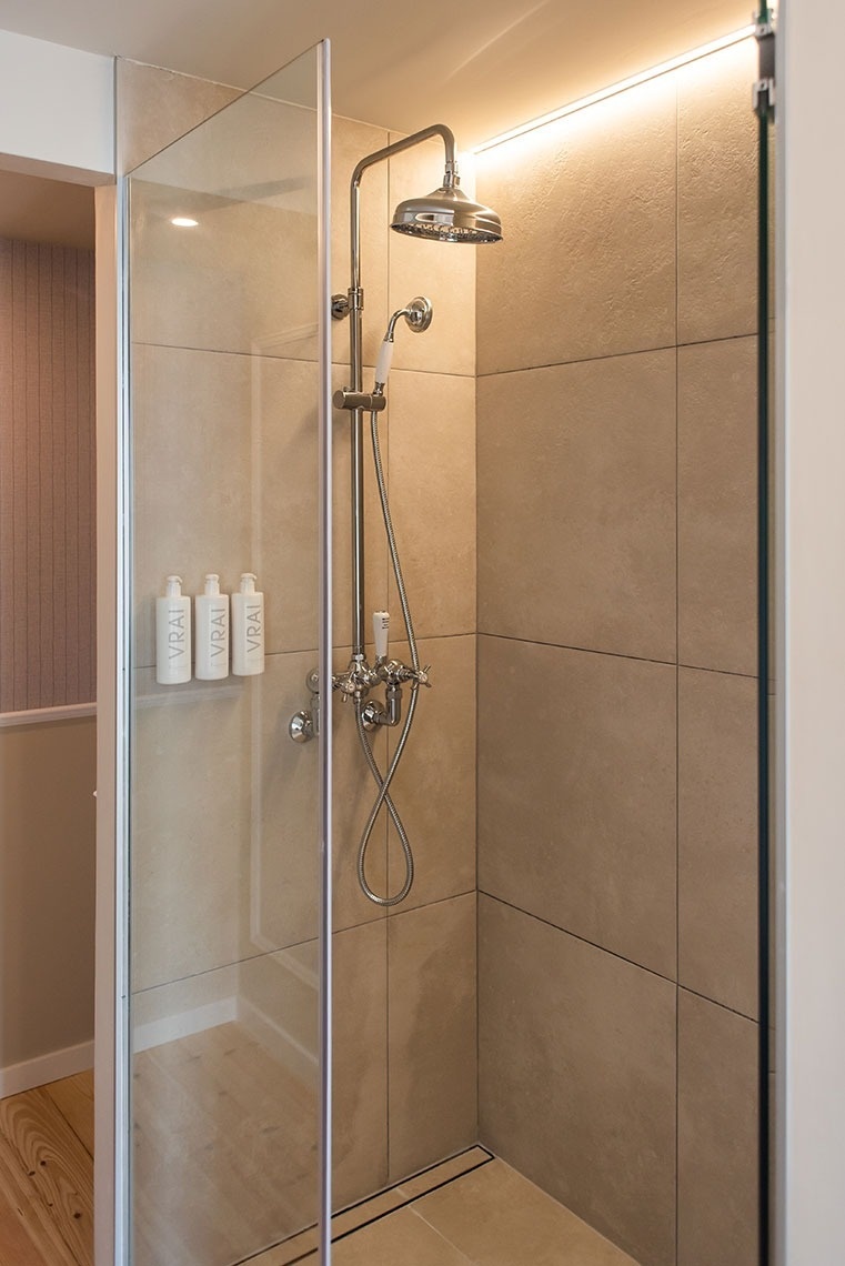 Chuveiro elegante de hotel com box de vidro, ducha tipo chuva e amenidades VRAI.
