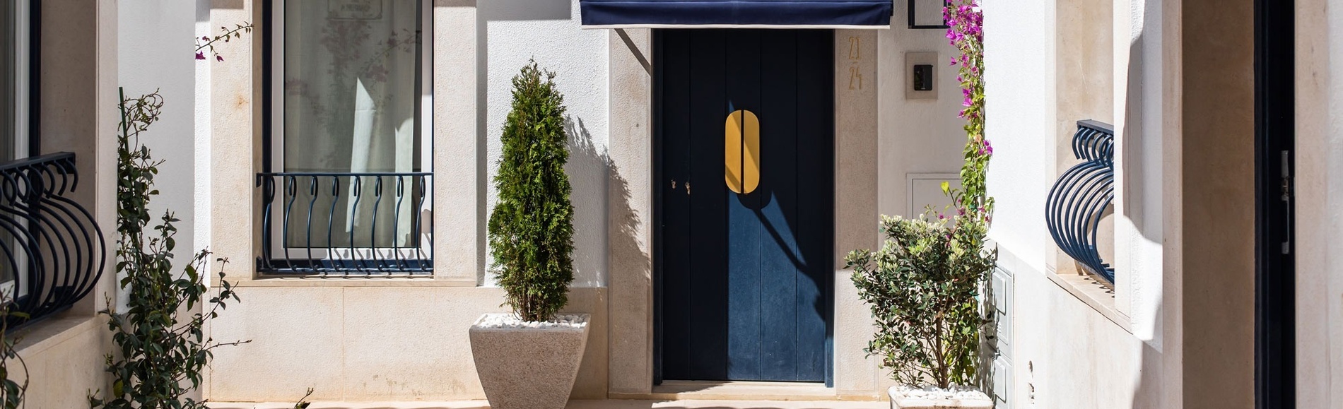 Fachada encantadora de hotel con puerta azul llamativa, tirador dorado y plantas en macetas soleadas.