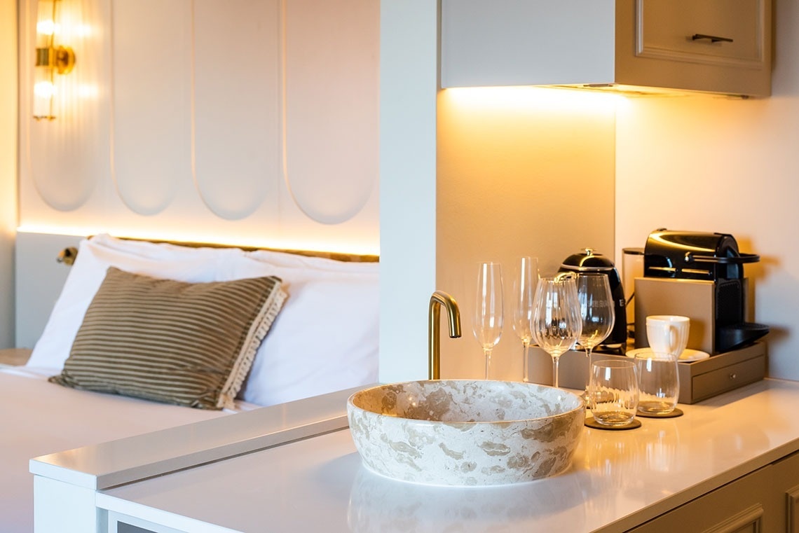 Suíte de hotel moderna com cama confortável, lavatório de design, cafeteira e copos.