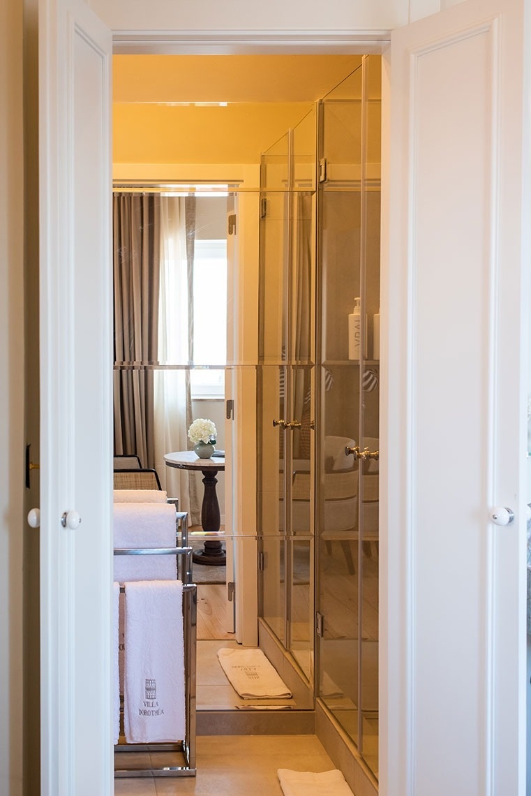 Banheiro de hotel elegante com ducha de vidro, toalhas felpudas e reflexo do quarto.