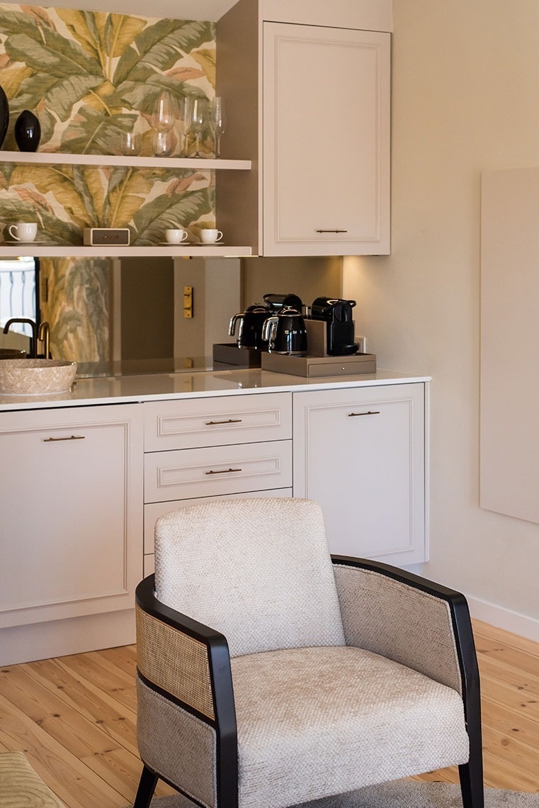 Quarto de hotel com kitchenette elegante, papel de parede tropical, máquina de café e poltrona confortável.