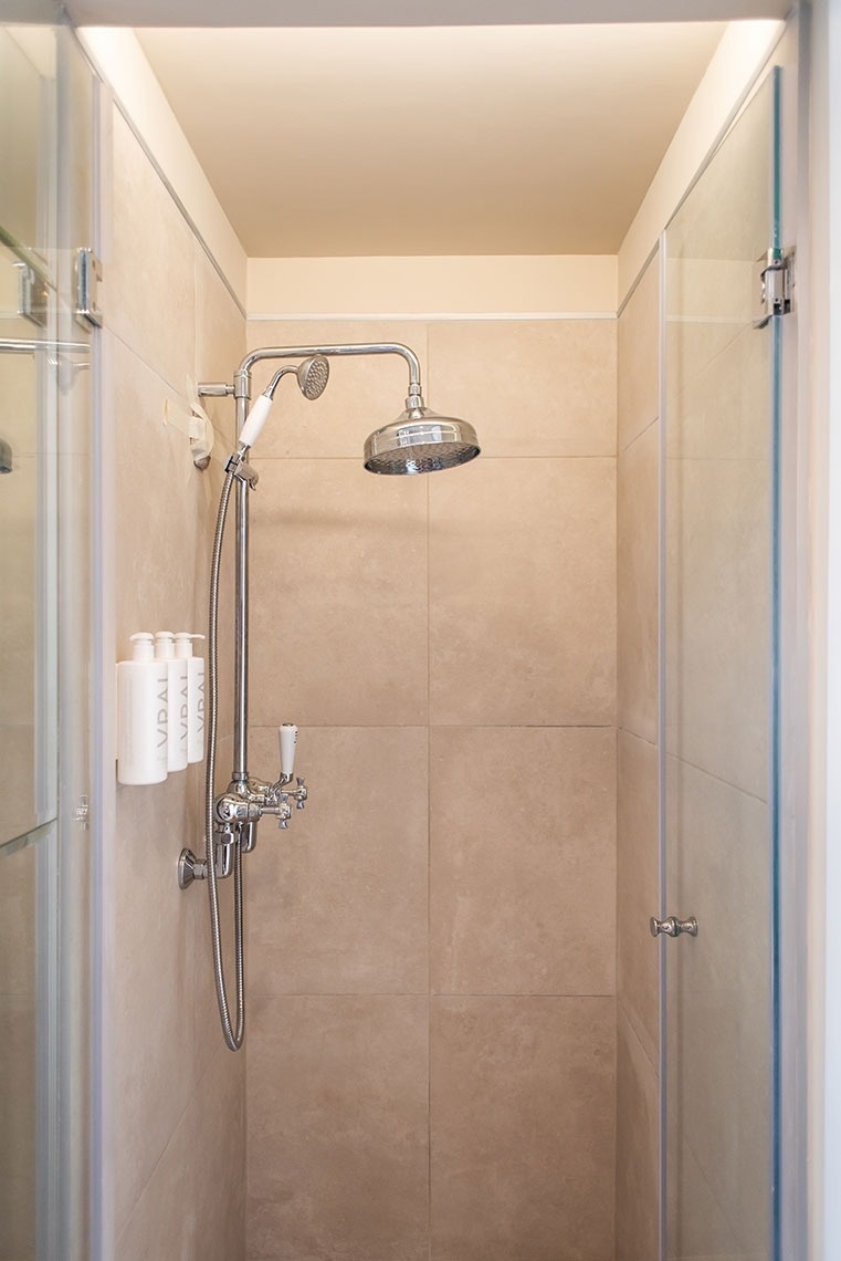 Chuveiro de design em quarto de hotel, com azulejos bege, chuveiros cromados e amenities Vidal.