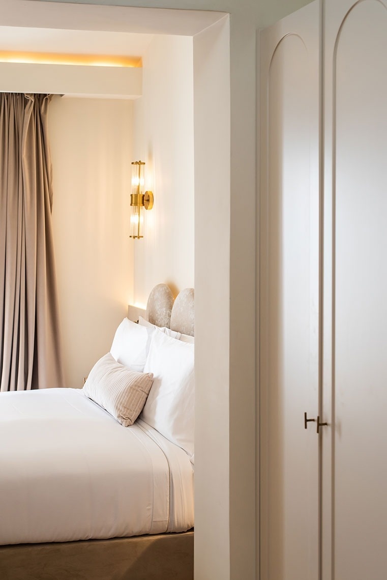 Quarto de hotel moderno com cama confortável, iluminação dourada e armário elegante.