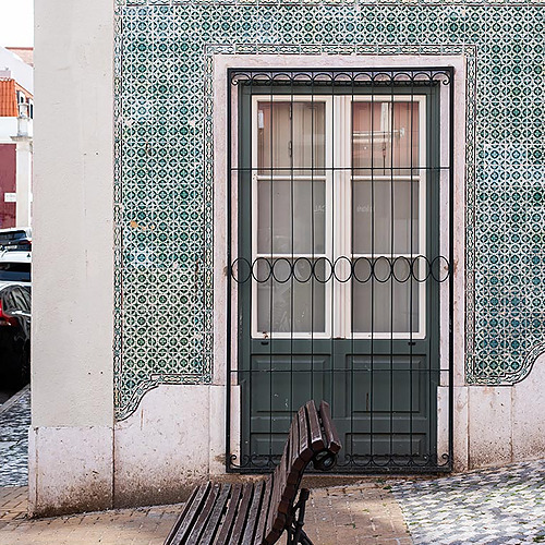 Banco de madera frente a puerta adornada con azulejos, ideal para alojamientos con encanto Villa Dorothea.