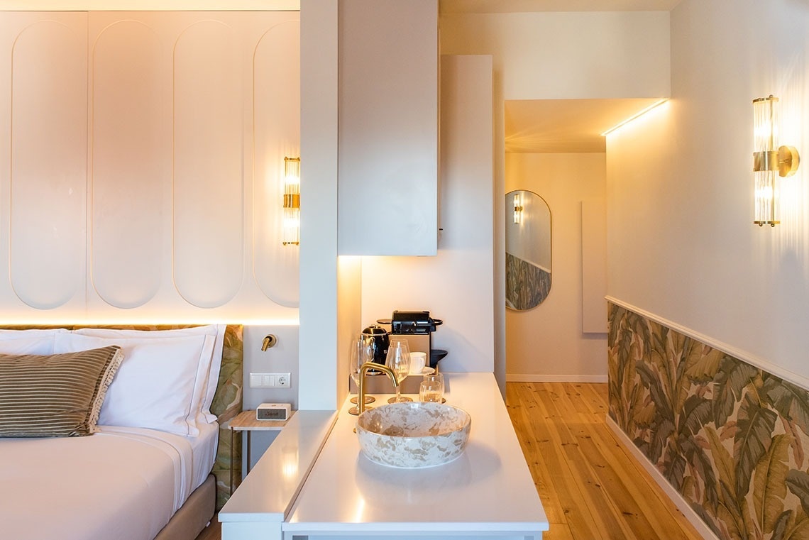 Suite de hotel moderna com cama, kitchenette, design botânico e iluminação acolhedora.