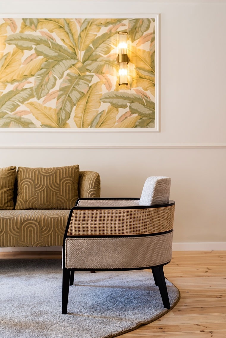 Quarto de hotel elegante: papel de parede com folhas tropicais, sofá moderno e poltrona de design em vime.