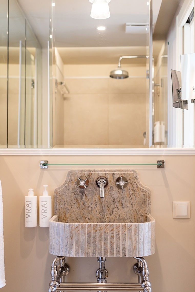 Banheiro luxuoso de hotel com pia de pedra moderna, torneiras cromadas e espelho amplo.