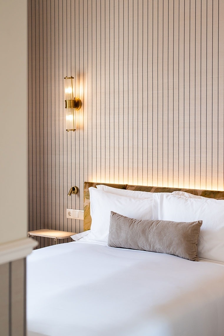 Quarto de hotel moderno com cama confortável, cabeceira iluminada e luminária de parede dourada.