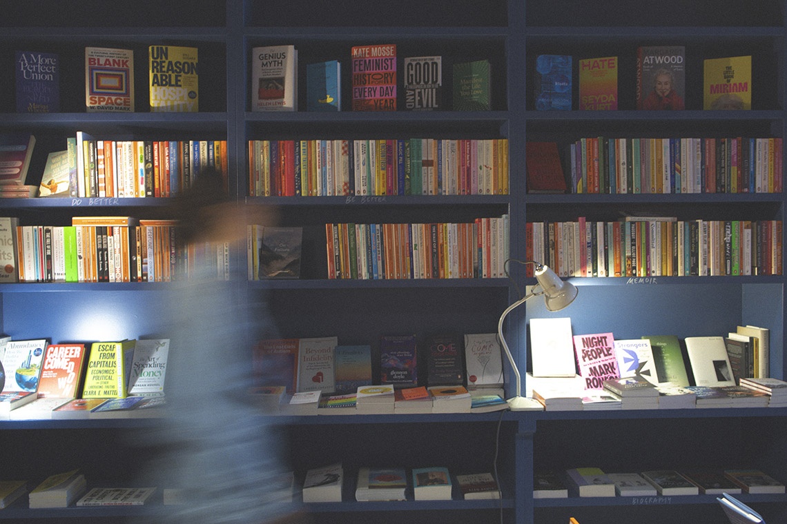 Livraria na Villa Dorothea com livros e luminária, ambiente aconchegante para relaxar.