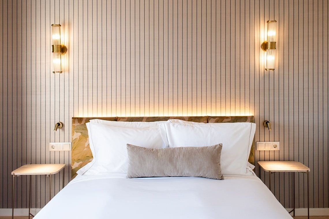 Quarto de hotel moderno e elegante, com cama confortável, cabeceira iluminada e detalhes dourados.