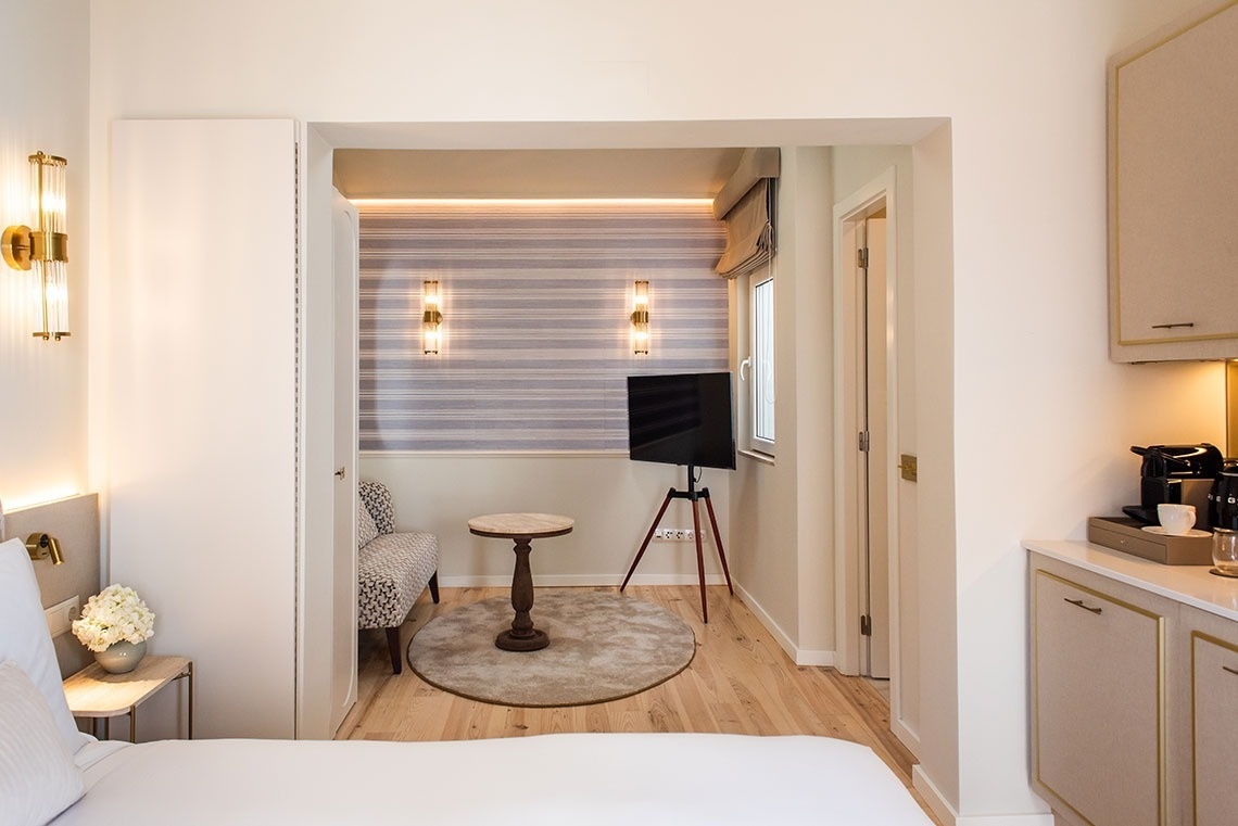 Quarto de hotel moderno com cama, aconchegante área de estar, TV e estação de café.