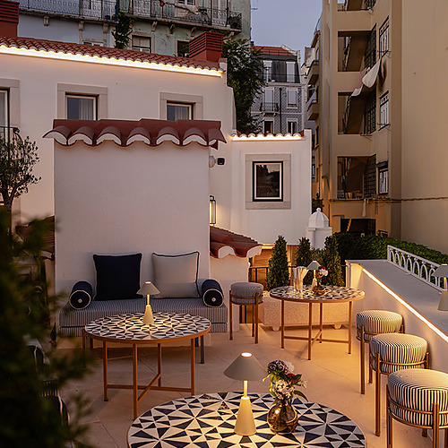 Terraza de hotel con mesas y sillones a rayas, iluminación tenue, vista urbana de Villa Dorothea