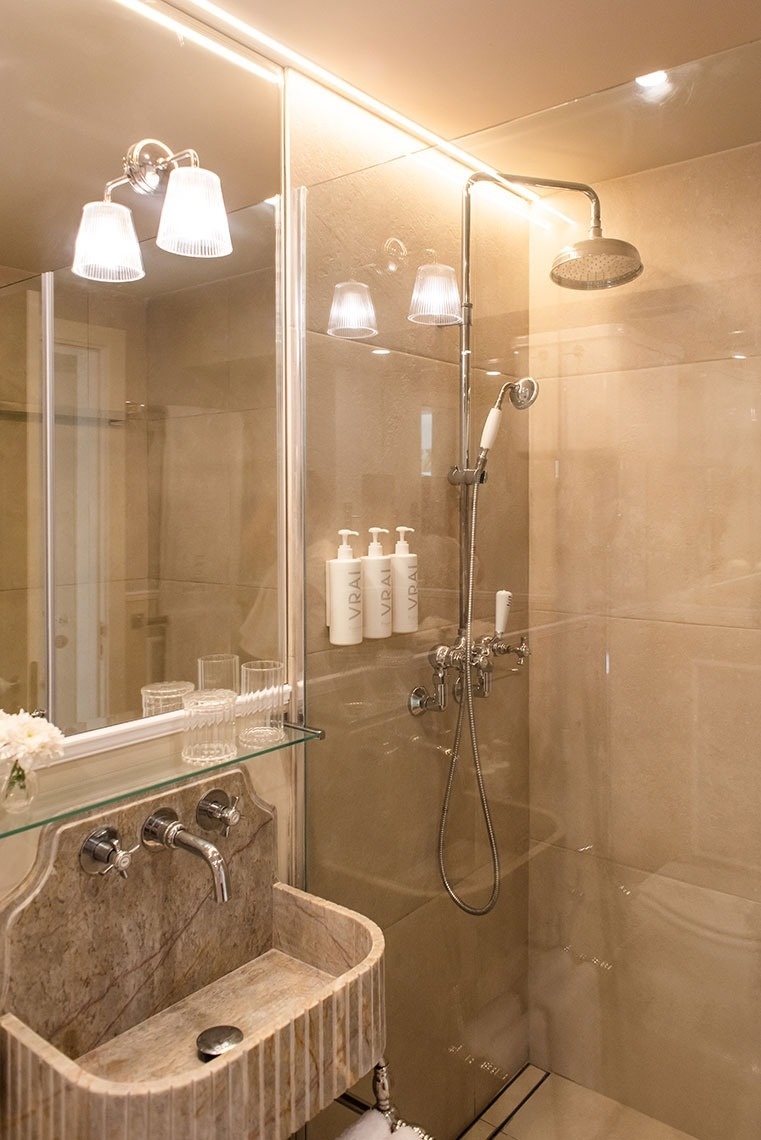 Banheiro de hotel moderno com chuveiro, pia de mármore esculpida e amenidades luxuosas.