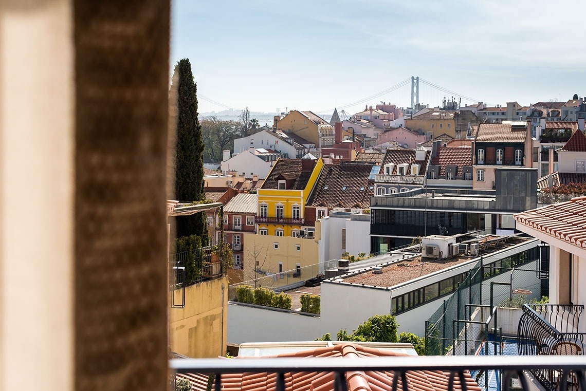 Vista da varanda do hotel em Lisboa: telhados e Ponte 25 de Abril ao sol.