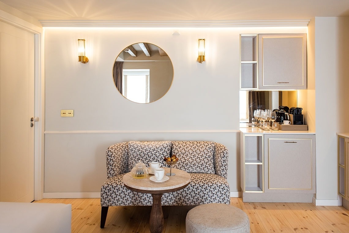 Suíte de hotel com área de estar confortável, decoração elegante, espelho, luminárias e minibar completo.