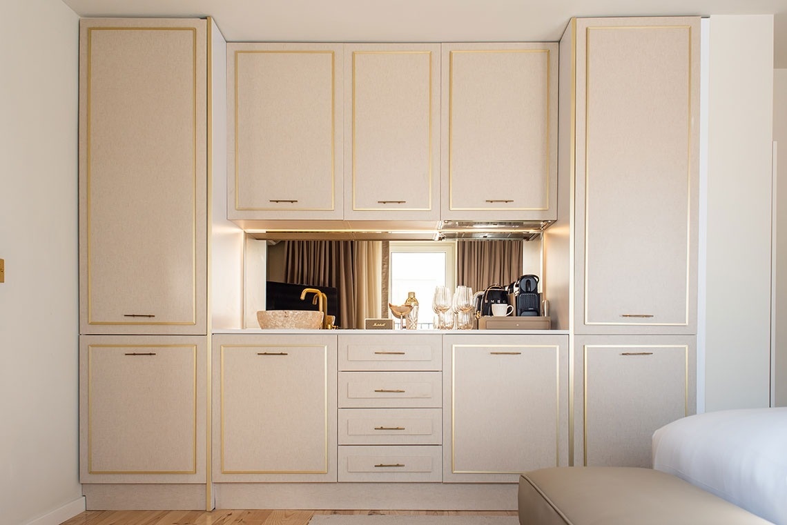 Kitchenette de hotel luxuosa: armários claros, detalhes dourados, pia, cafeteira e minibar integrado.