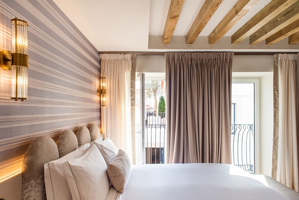 Quarto de hotel moderno com cama confortável, vigas de madeira, papel de parede listrado e varanda.