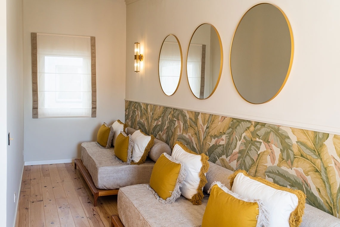 Alojamento hotel boutique: daybeds, espelhos dourados, papel parede botânico e almofadas amarelas.