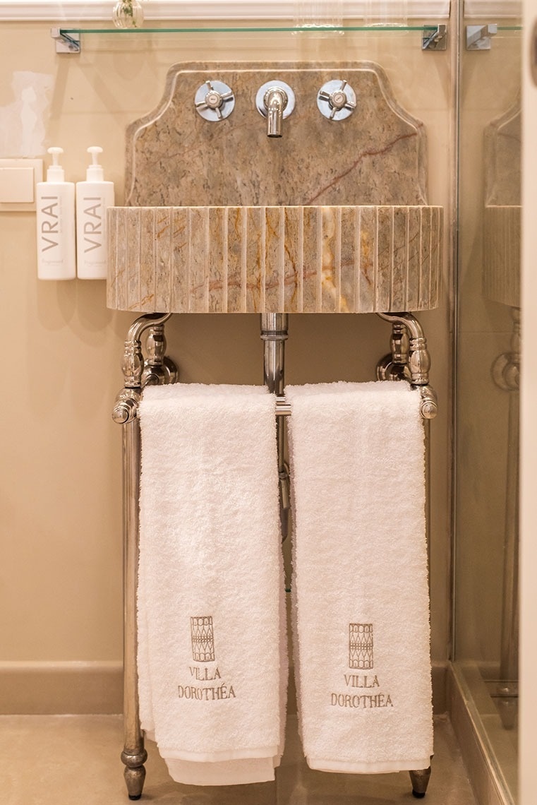 Banheiro luxuoso com pia de mármore, torneira vintage e toalhas personalizadas Villa Dorothea.