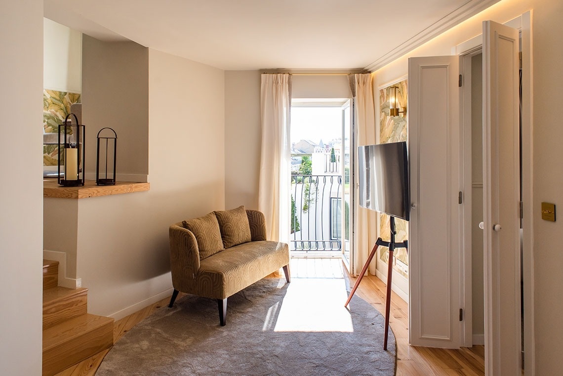 Elegante sala de estar de hotel com sofá confortável, TV, acesso à varanda e luz natural.