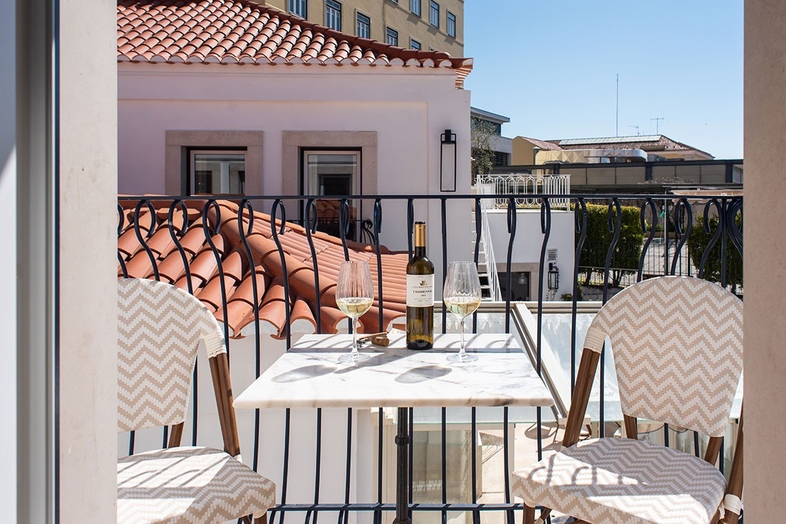 Varanda de hotel relaxante com vinho, mesa e cadeiras, com vista para a cidade.