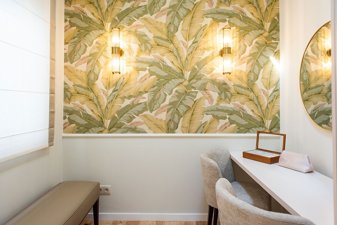 Quarto de hotel com papel de parede tropical, penteadeira, espelho, e iluminação elegante.