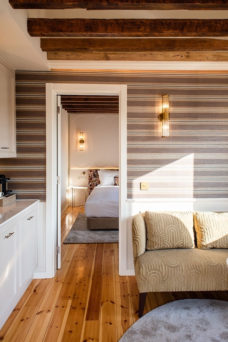 Suíte de hotel elegante com área de estar aconchegante, vigas de madeira expostas e vista para o quarto.