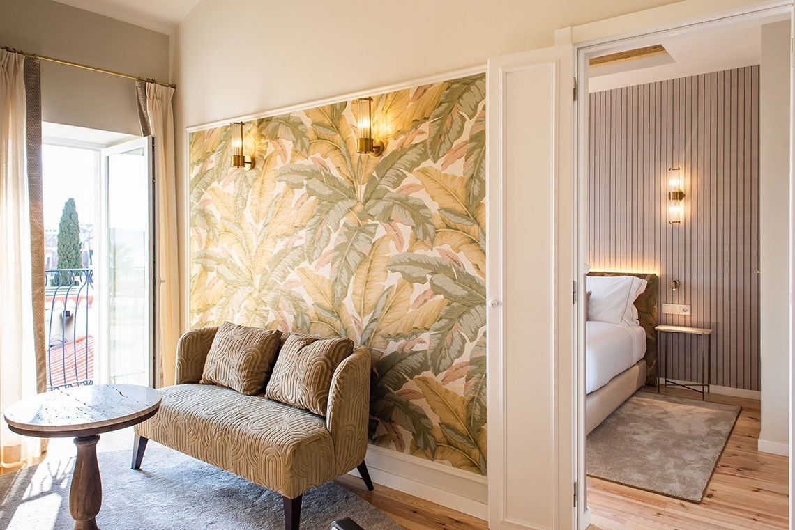 Suíte de hotel moderna com sala de estar, varanda, papel de parede tropical e quarto confortável.