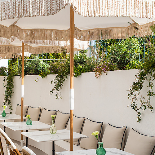 Terraza de Villa Dorothea: mesas de mármol, cojines beige y sombrillas con flecos.
