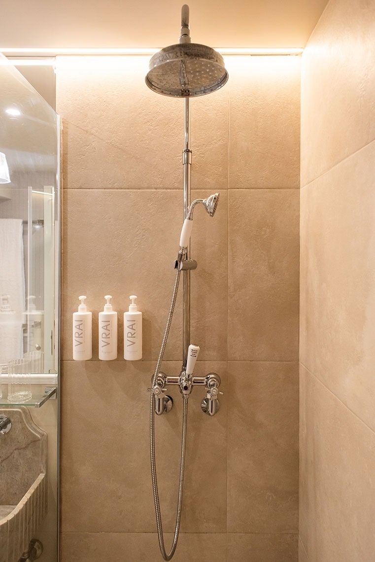 Chuveiro moderno com efeito chuva, chuveirinho e amenities VRAI em banheiro de hotel elegante.