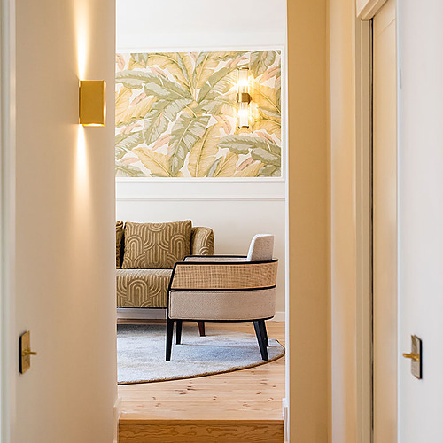 Pasillo en Villa Dorothea con papel tapiz botánico y sillón de mimbre.