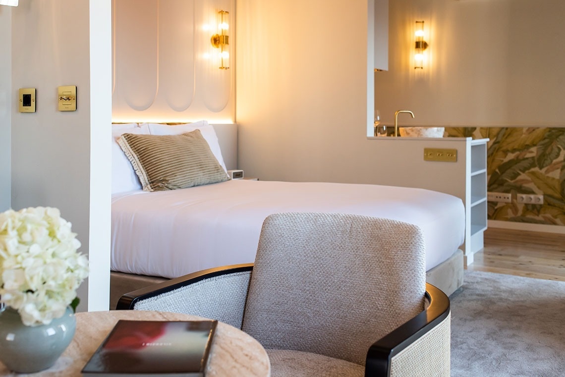 Quarto de hotel elegante e moderno com cama confortável, kitchenette e detalhes dourados.
