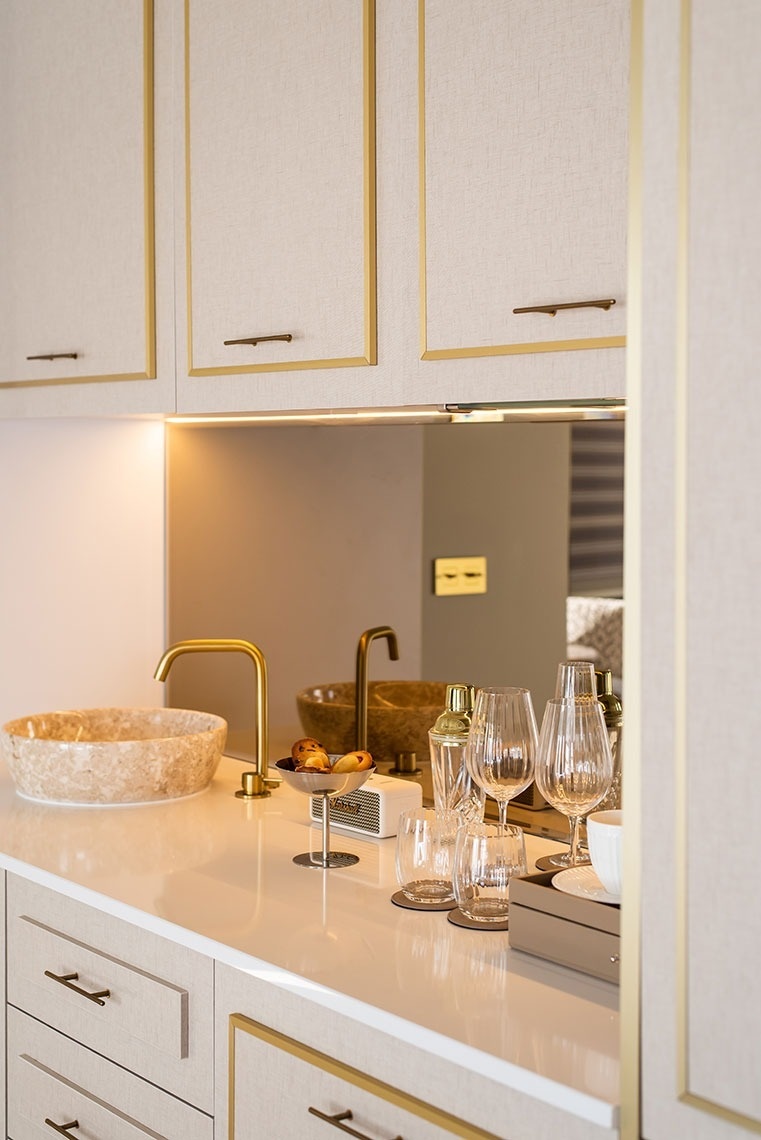 Mini-bar luxuoso em suíte de hotel com detalhes dourados, pia de pedra e copos.