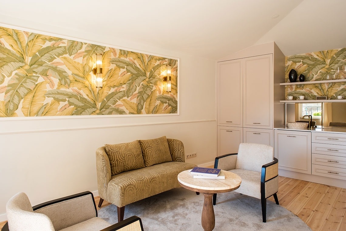 Suíte de hotel com área de estar tropical, sofá, poltronas e kitchenette.