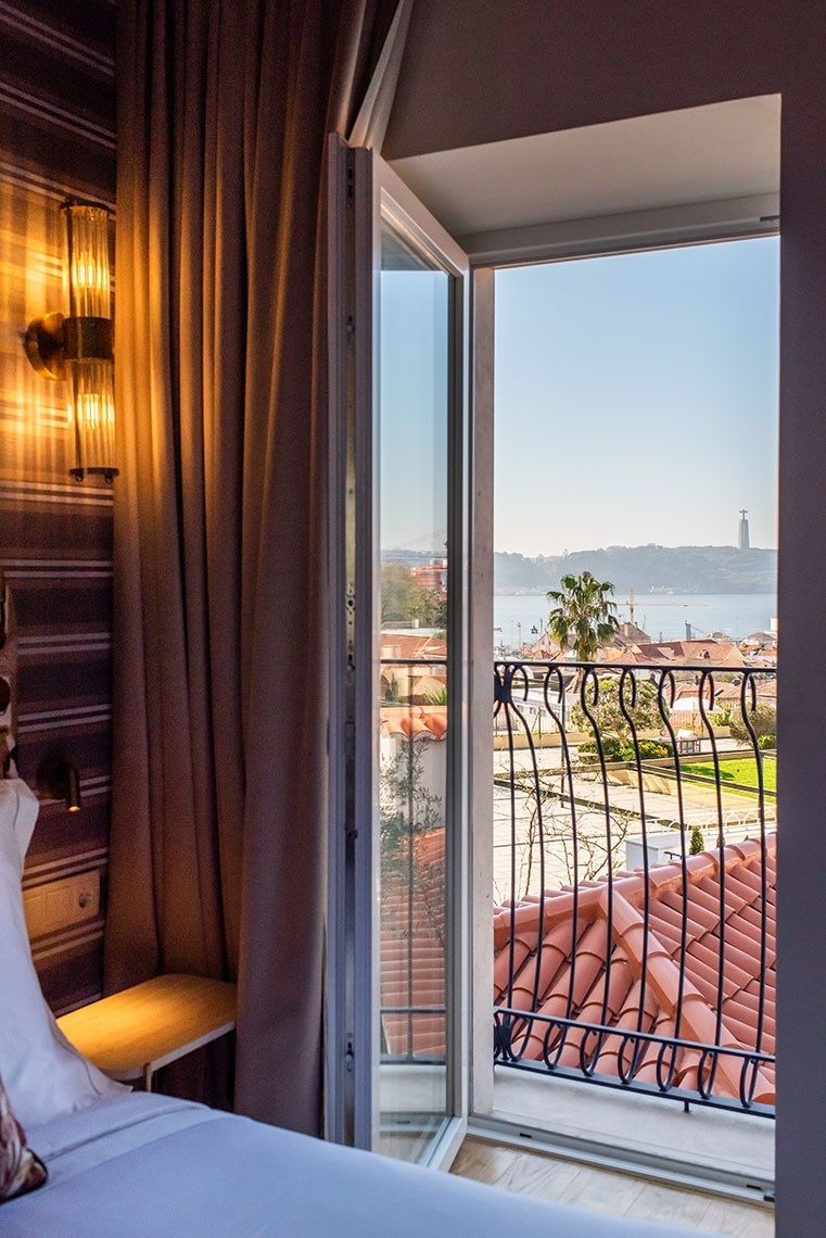 Quarto de hotel confortável com vista para o Rio Tejo, Cristo Rei e Lisboa, através de uma varanda com telhados.