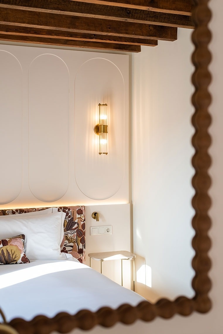Quarto de hotel moderno com cama confortável, cabeceira estampada, iluminação elegante e teto de madeira.