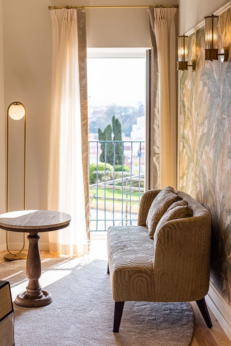 Quarto de hotel com varanda, sofá elegante, mesa lateral, luminária e vista panorâmica.