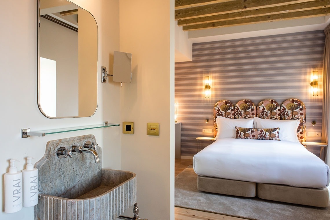 Quarto de hotel moderno com cama king-size, cabeceira de design e banheiro elegante com pia de pedra.
