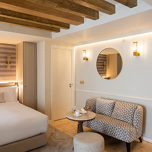 Habitación de lujo en Villa Dorothea con cama confortable, sofá elegante y espejo redondo.
