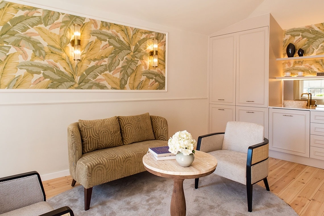 Aconchegante área de estar em suíte de hotel com design tropical, sofá, poltronas, mesa de centro e minibar.