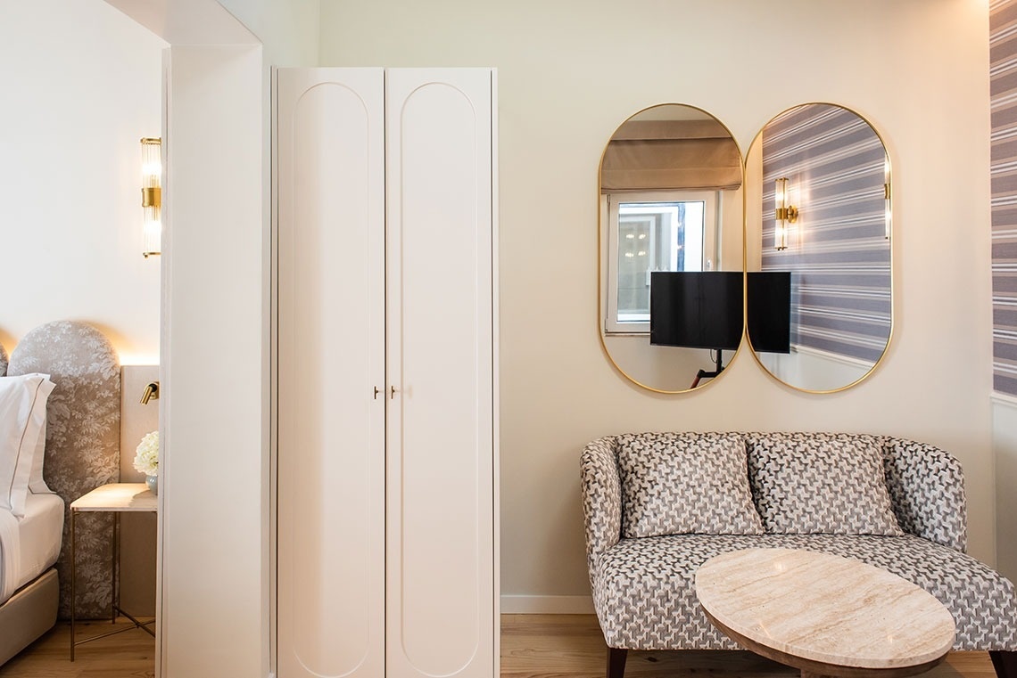 Quarto de hotel moderno com sofá estampado, espelhos ovais dourados e guarda-roupa. Alojamento elegante.