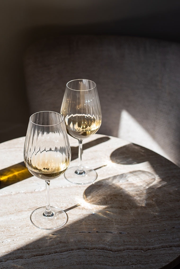 Duas taças de vinho branco na mesa do hotel com luz natural e sombras.