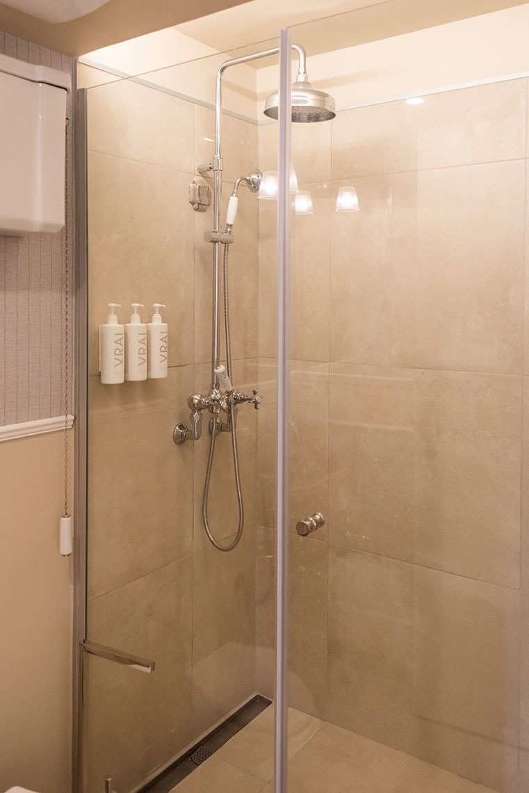 Banheiro de hotel com chuveiro de luxo, box de vidro e produtos de banho.