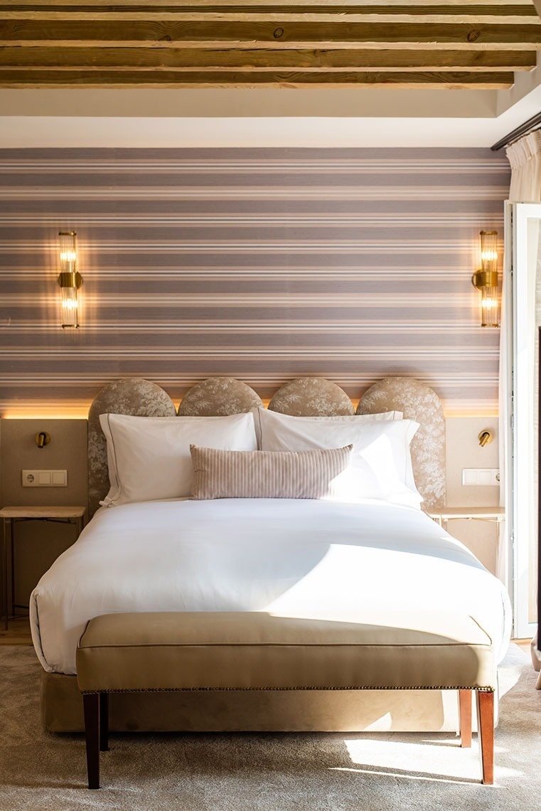 Quarto de hotel moderno com cama king-size, vigas de madeira e iluminação aconchegante.