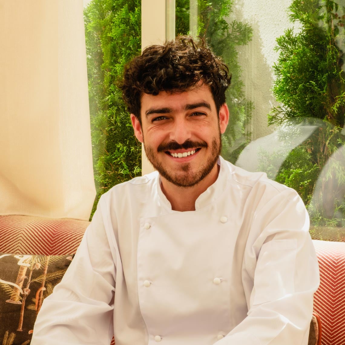 Chef sonriente con uniformeVilla Dorothea en un restaurante de hotel, rodeado de vegetación.
