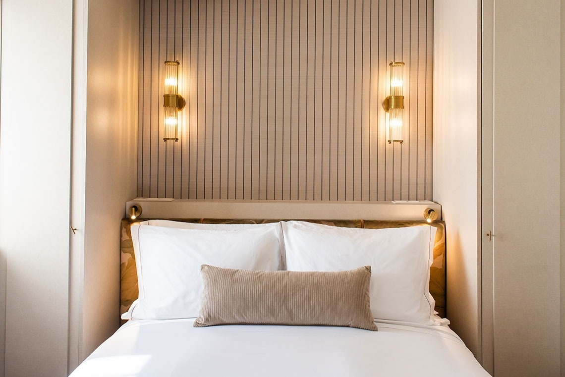 Quarto de hotel moderno com cama aconchegante, iluminação ambiente e detalhes elegantes.
